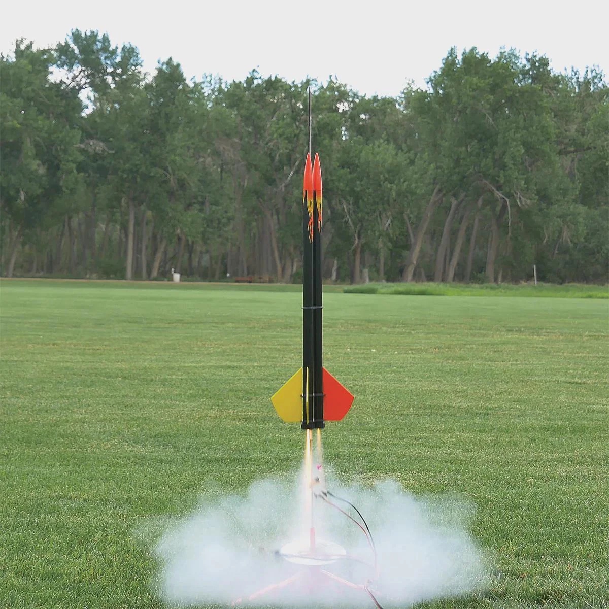 Model rocket lifting off from a launch pad in an open field